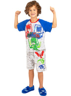 Berniukas su „PJ Masks“ pižama, mėlynomis rankovėmis ir šlepetėmis balto fono fone.