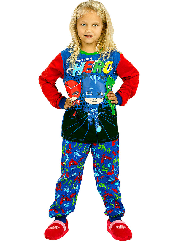 Šviesiaplaukė mergaitė su spalvota „PJ Masks“ pižama ir raudonomis šlepetėmis.