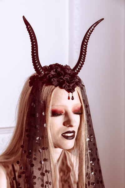 Person wearing a headpiece with large horns and a sheer black veil against a white background