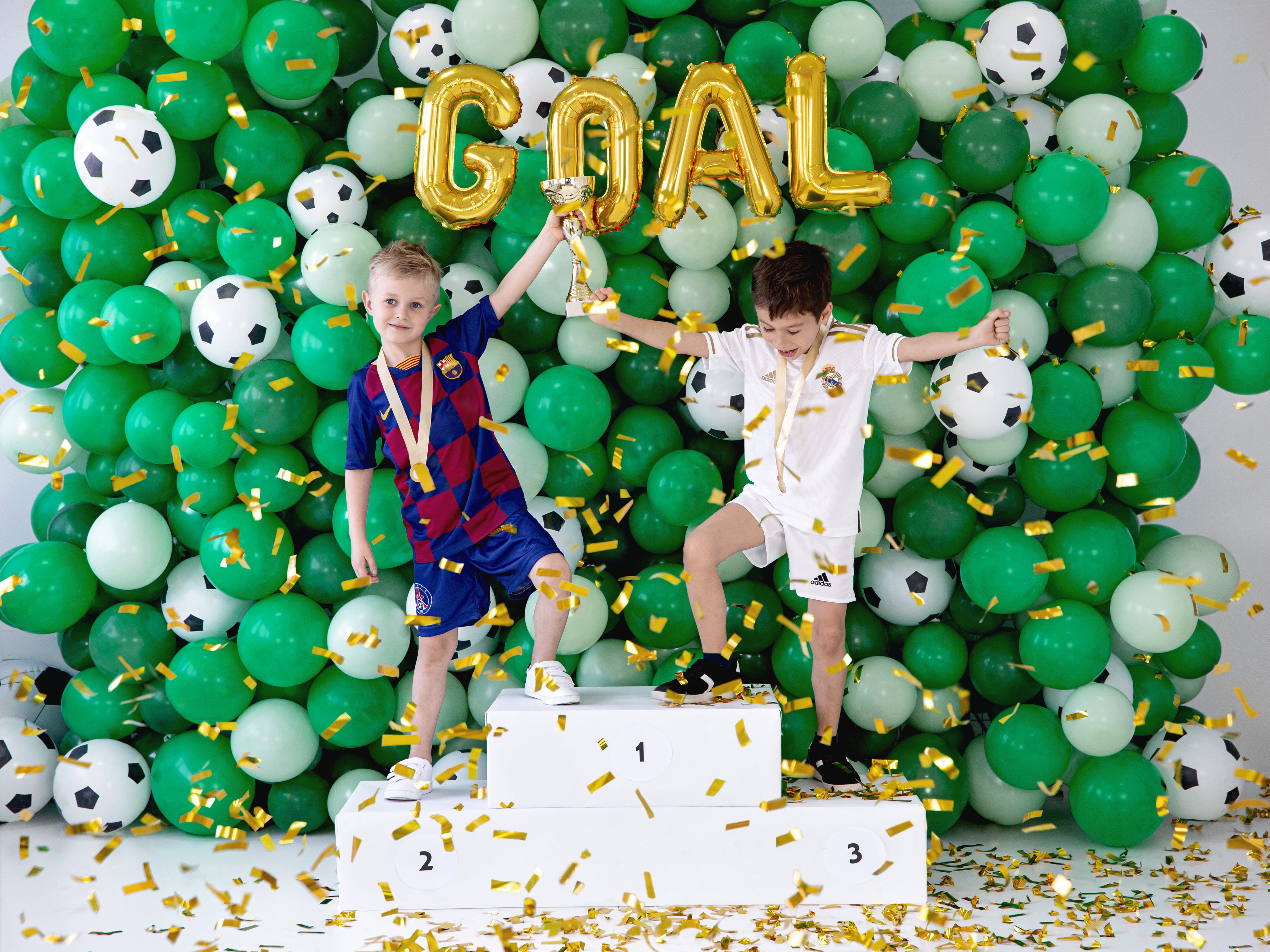 Two children on a podium with a 'GOAL' balloon and soccer ball decorations.