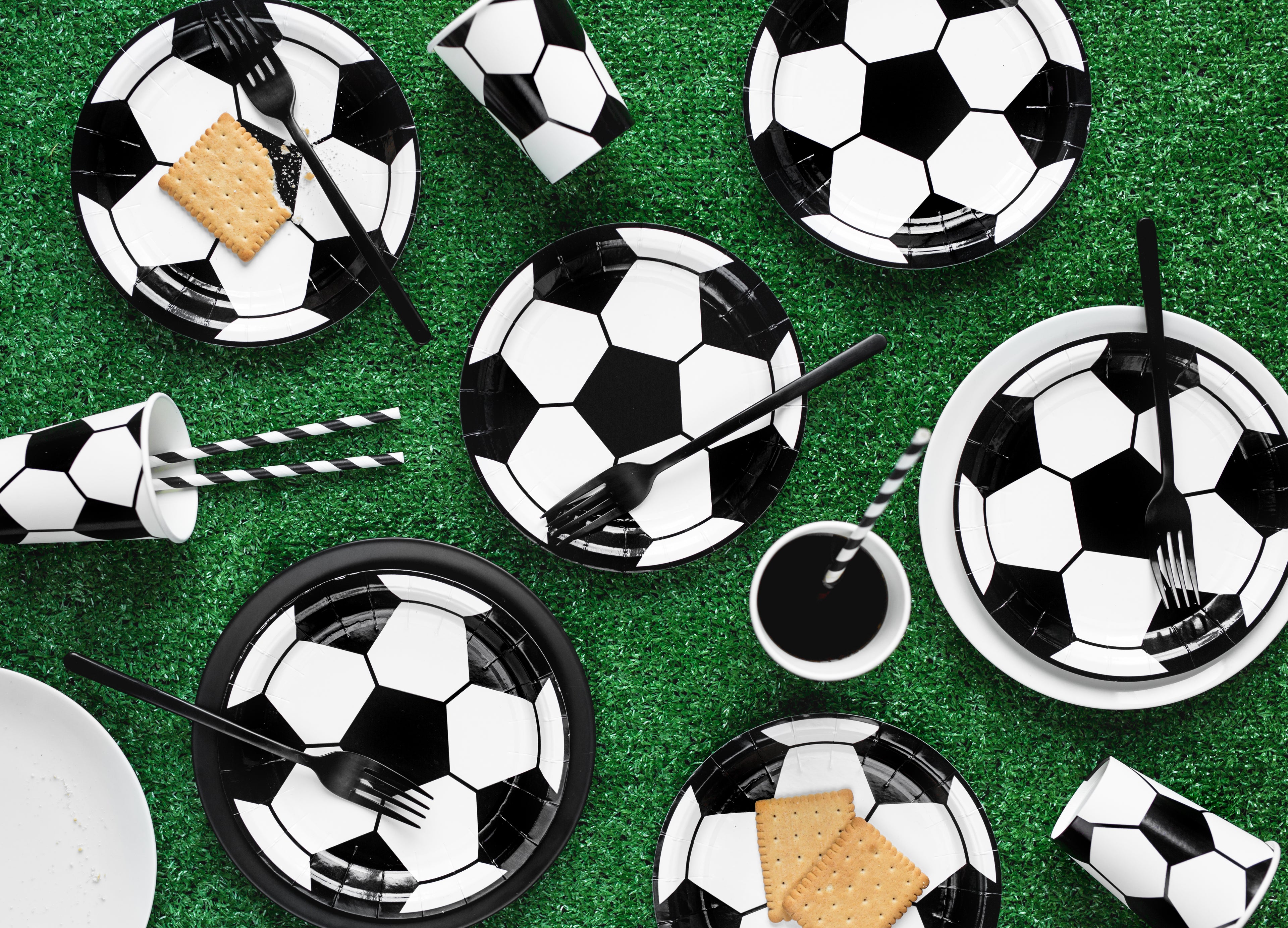 Soccer-themed party supplies including plates, cups, and cutlery on a green surface.