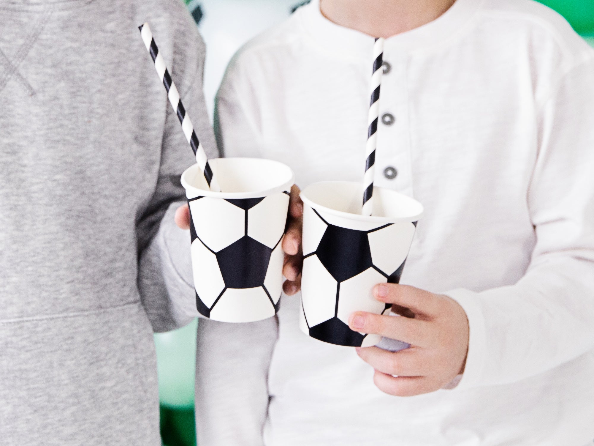 Two children holding soccer-themed paper cups with straws.