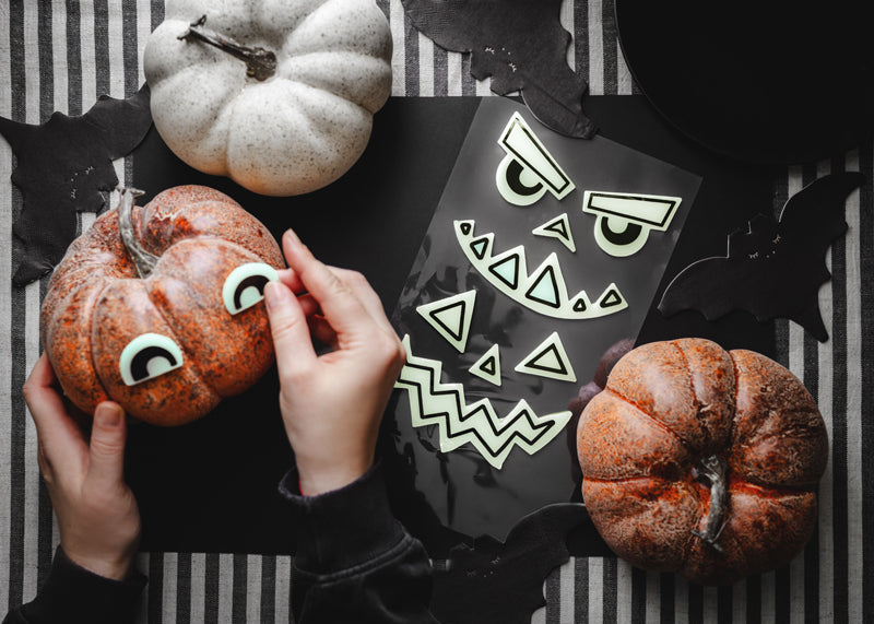 Person decorating pumpkins with face stickers on a striped background