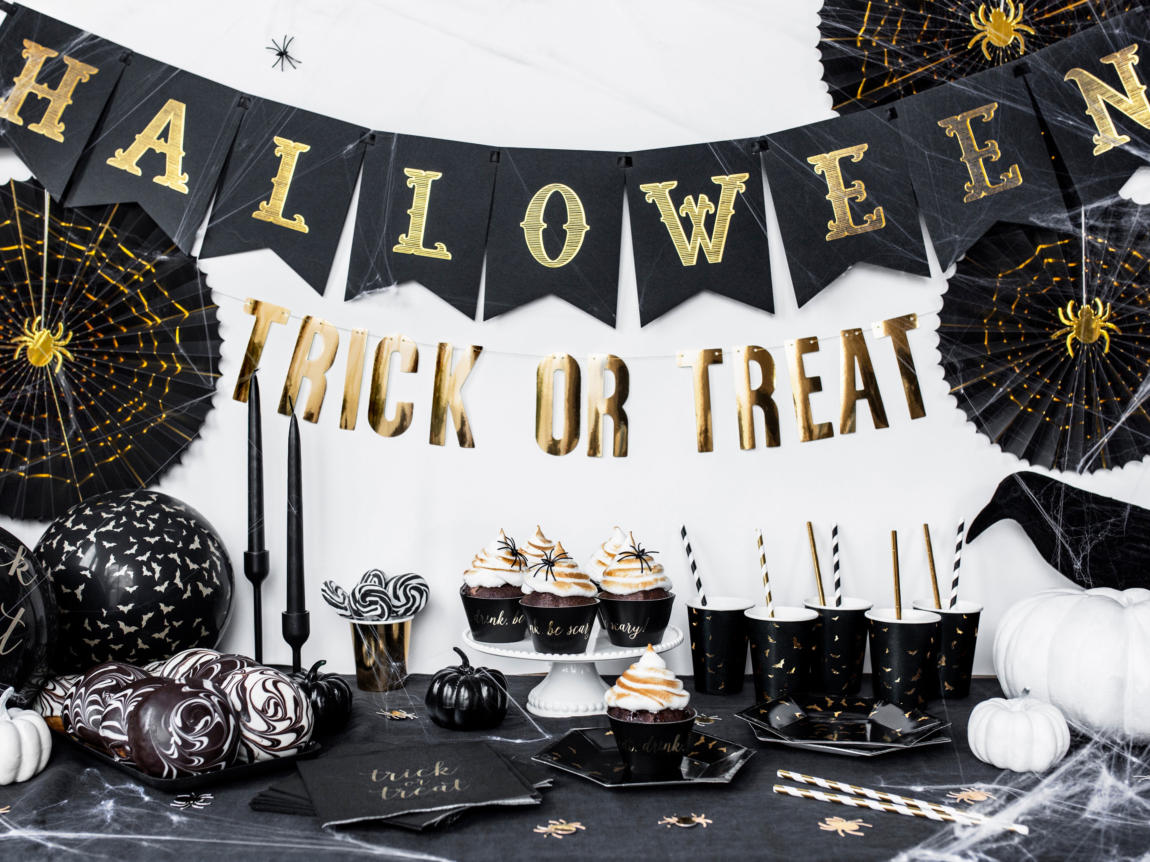 Halloween-themed table setting with 'Trick or Treat' banner and black and gold decorations.