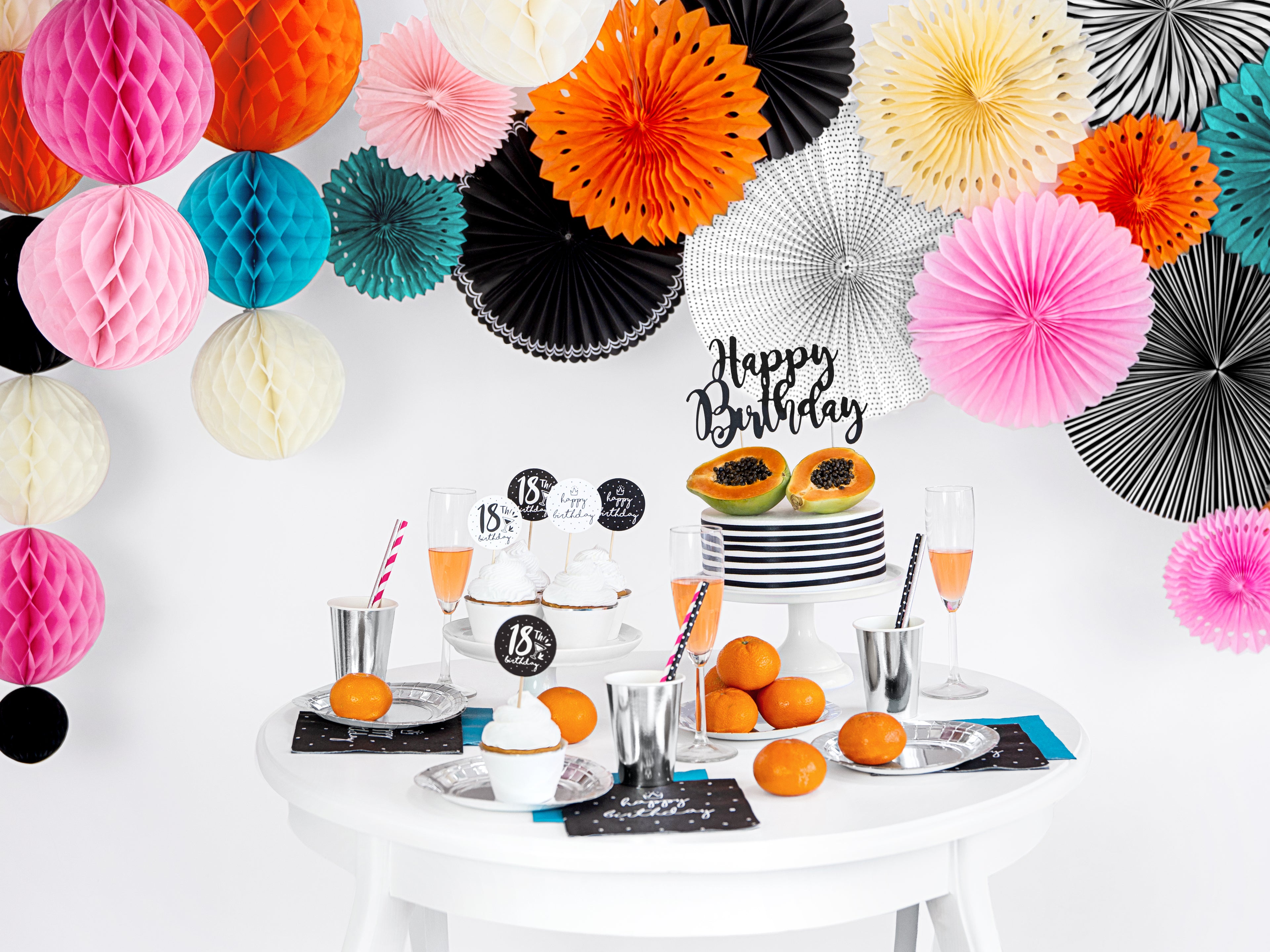 Birthday party setup with colorful paper fans and a table with food and drinks.