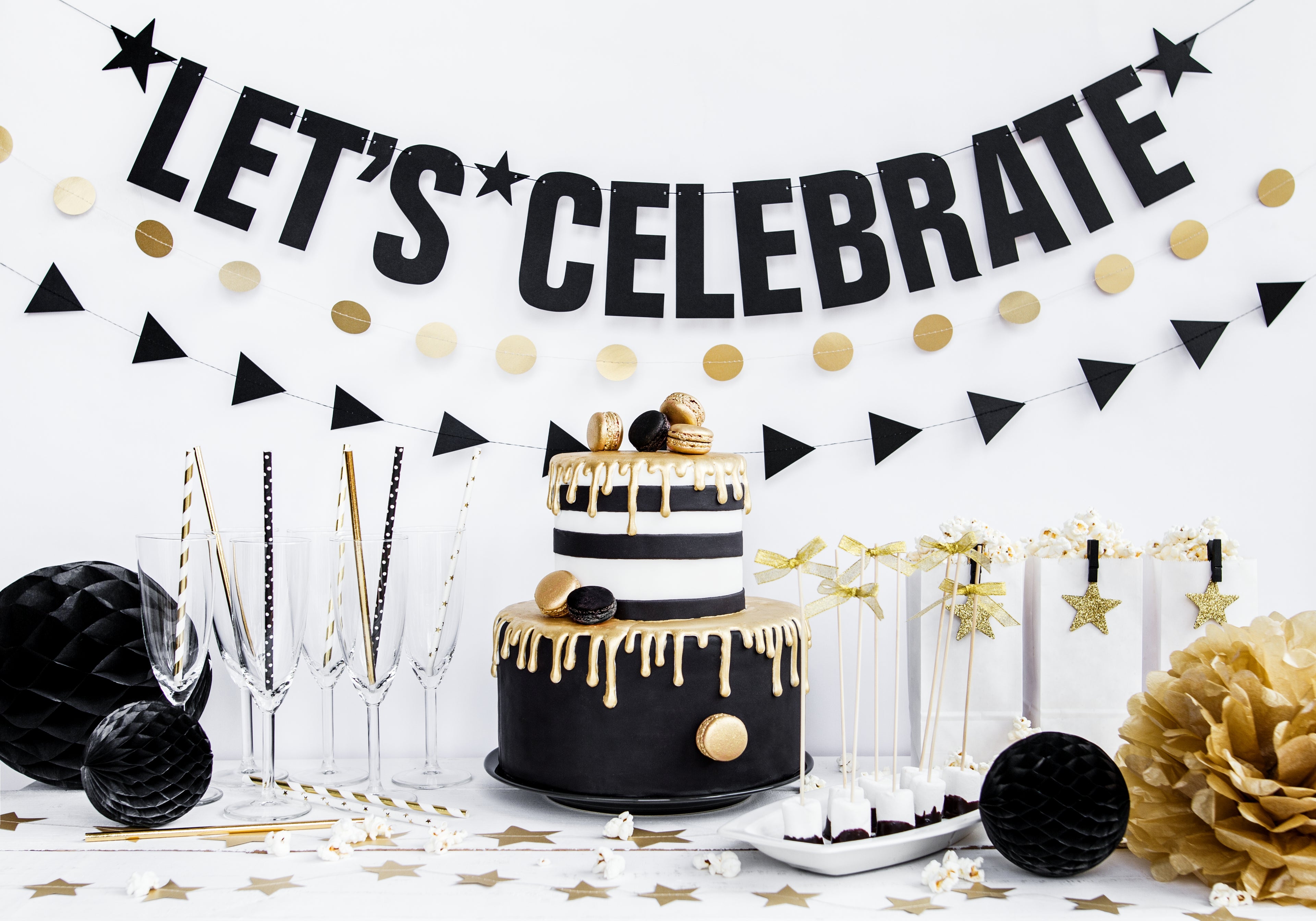 Black and gold cake with 'Let's Celebrate' banner and decorative elements on a white background