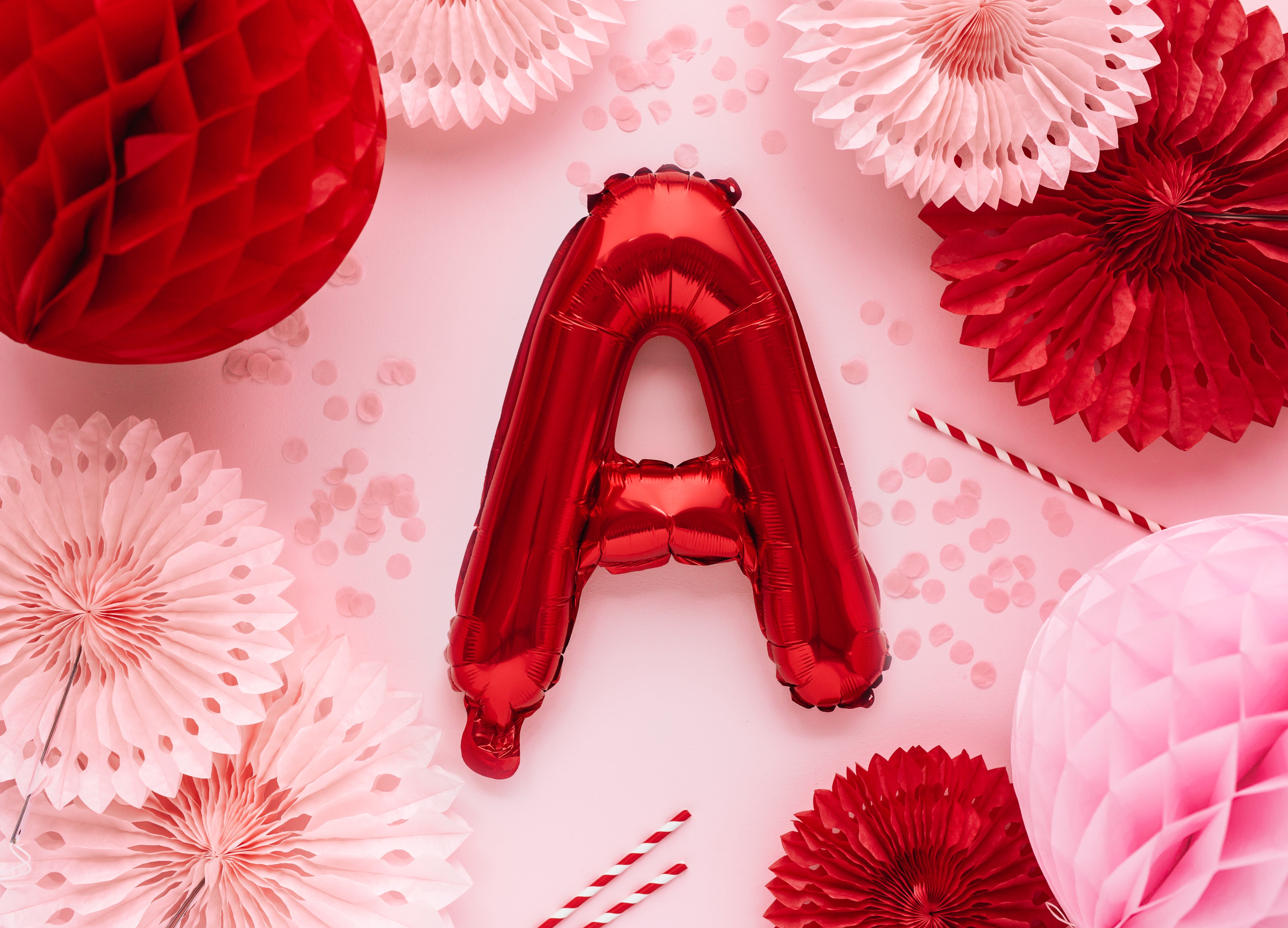 Red letter 'A' balloon surrounded by pink and red paper decorations on a pink background