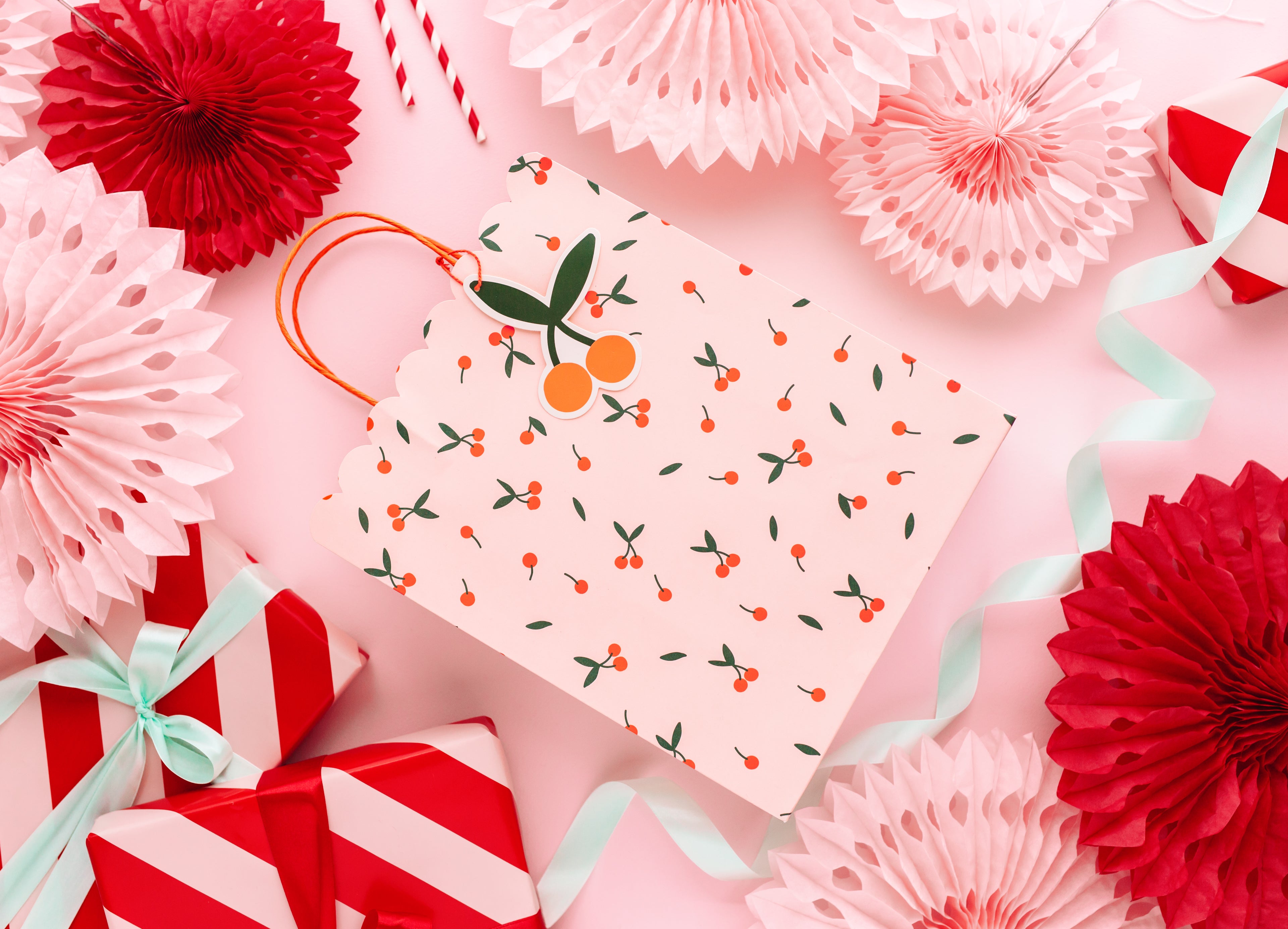 Gift tag with cherry design surrounded by red and pink paper flowers on a pink background