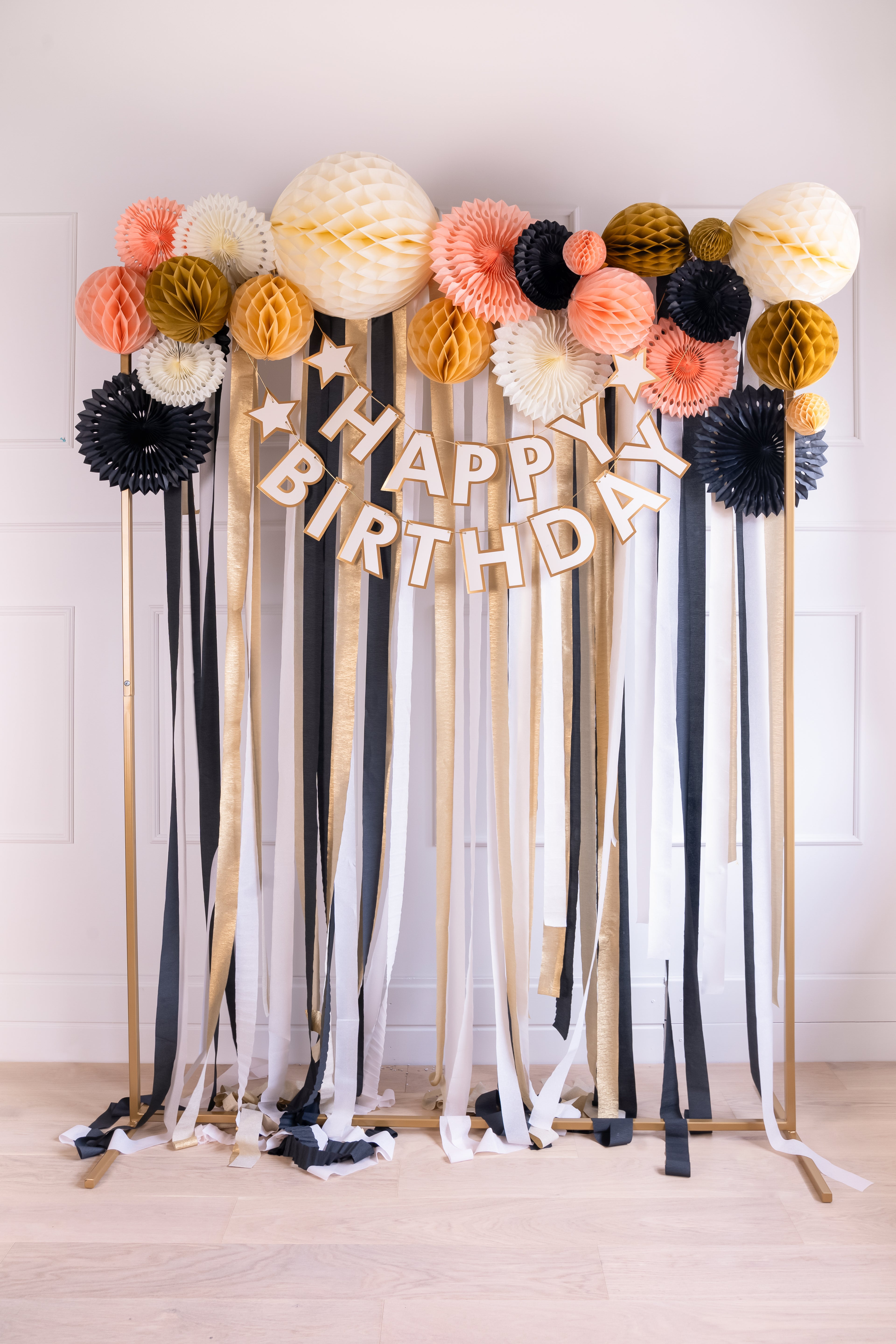 Decorative birthday backdrop with colorful balloons and ribbons on a white wall.