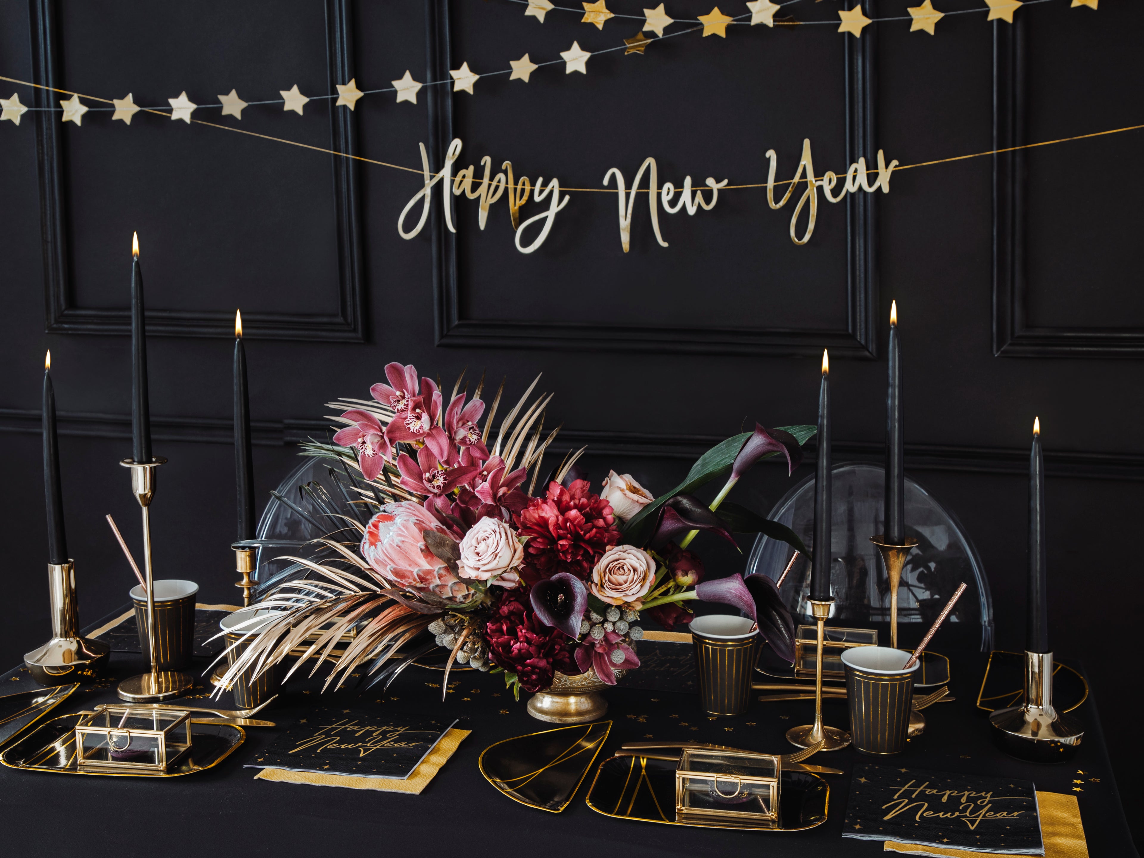 Decorative table setting with flowers, candles, and 'Happy New Year' banner on a dark background