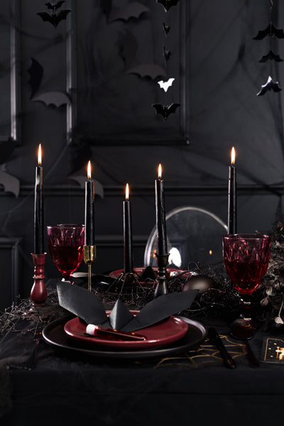 Halloween-themed table setting with black candles, red glasses, and dark decor.
