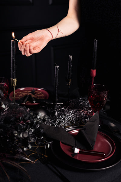 Darkly themed table setting with a hand lighting a candle.