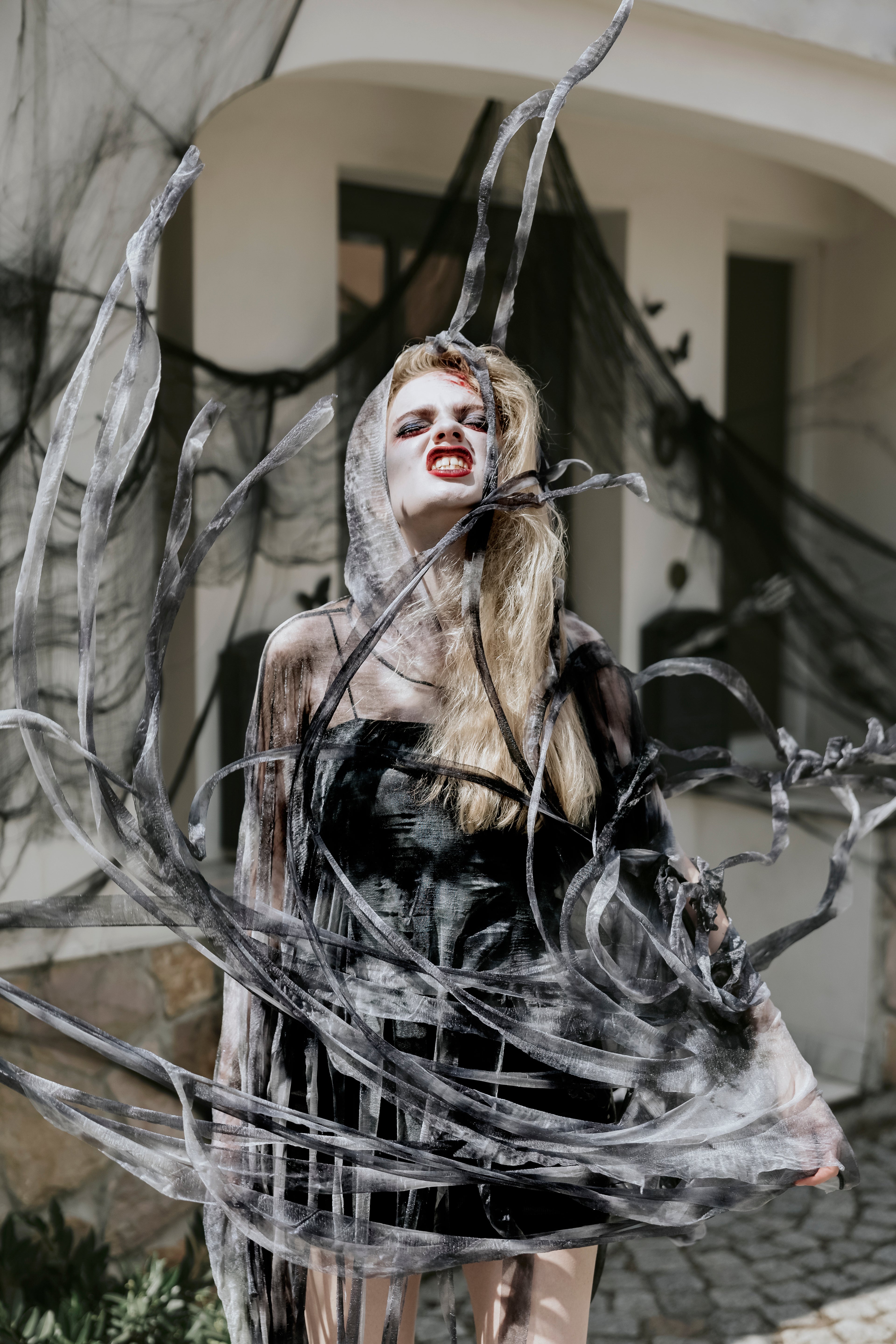 Person in a black dress with spider webs and branches in an outdoor setting
