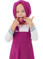 Maža mergaitė su violetine skarele ir suknele rodo liežuvį baltame fone.