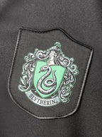 „Slytherin“ koledžo herbas su gyvate žaliame fone ant juodo audinio.