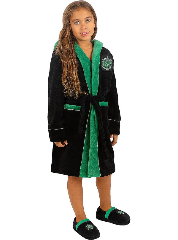 Mergaitė su juodai žaliu „Slytherin“ chalatu ir šlepetėmis baltame fone.